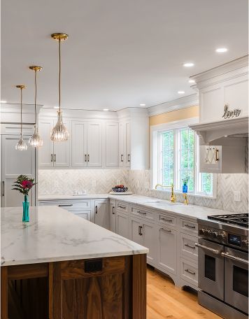 Remodeled kitchen with white marble countertops and set of three casement windows with grids over the sink.