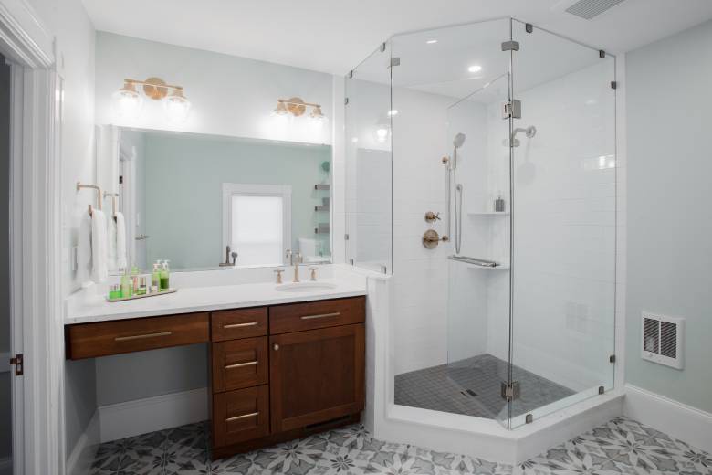 Remodeled primary bathroom with glass-enclosed shower and dark wood vanity with white countertop.