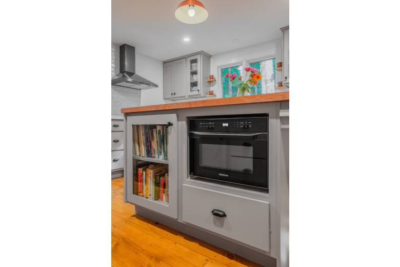 a microwave and cookbook storage built into the side of a kitchen counter