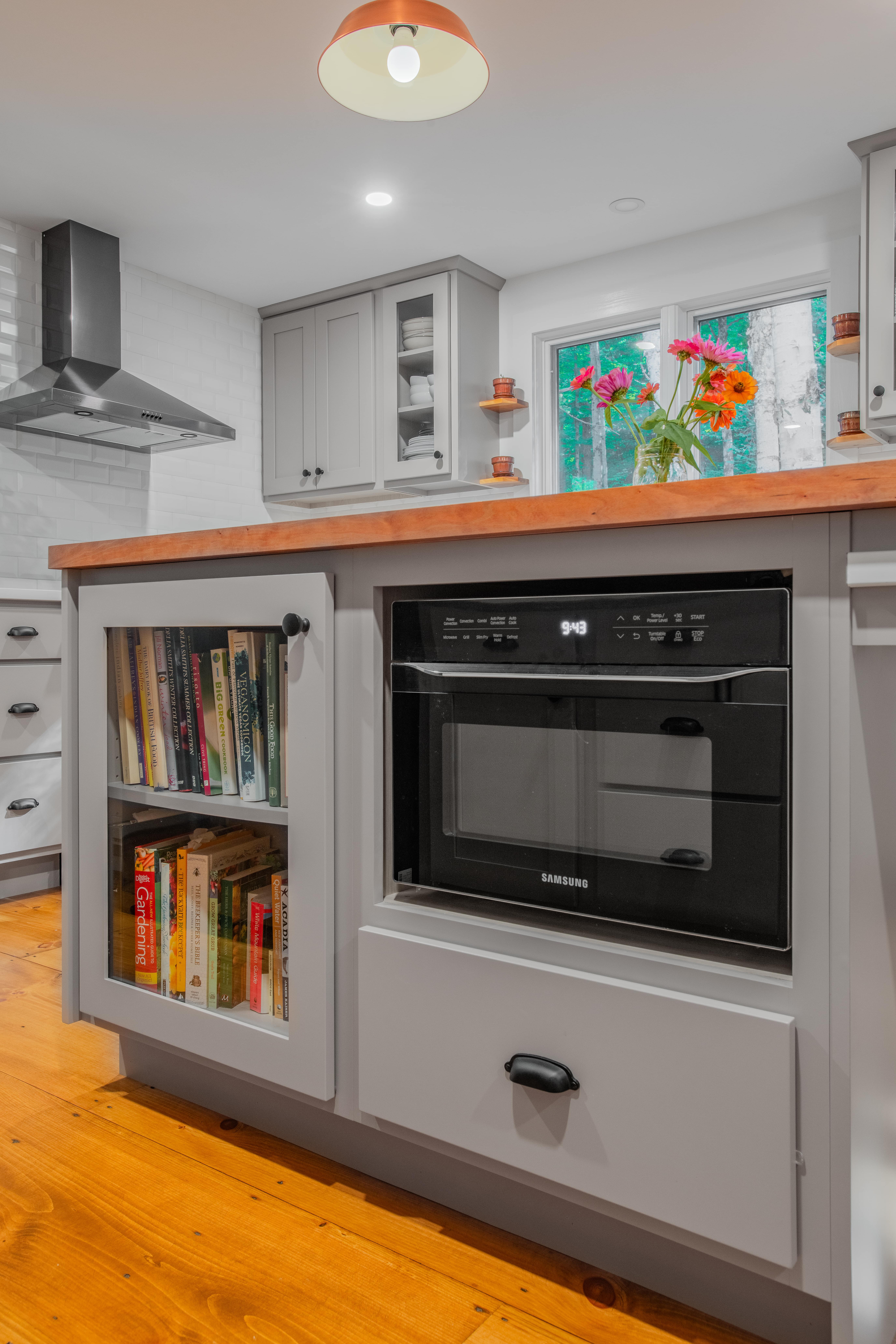 a microwave and cookbook storage built into the side of a kitchen counter