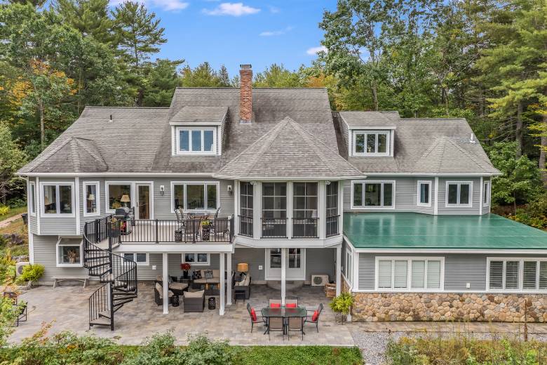 An aerial view of a large house with an upper deck and patio, surrounded by trees in background.