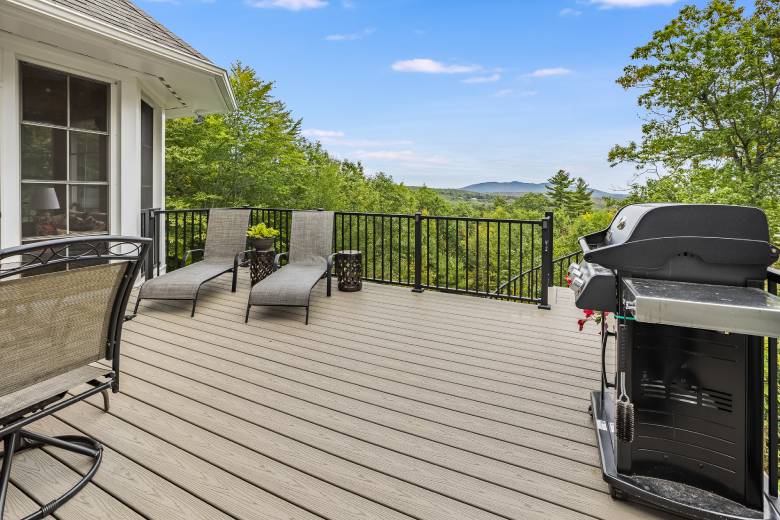 a grill and chaise lounges on a wooden deck