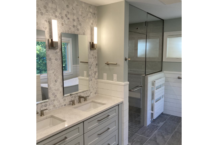 Modern bathroom remodel with glass-enclosed shower, dual vanities with white countertop, and gray large-tile flooring.
