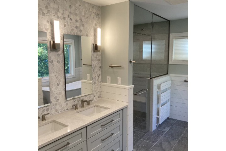 Modern bathroom remodel with glass-enclosed shower, dual vanities with white countertop, and gray large-tile flooring.