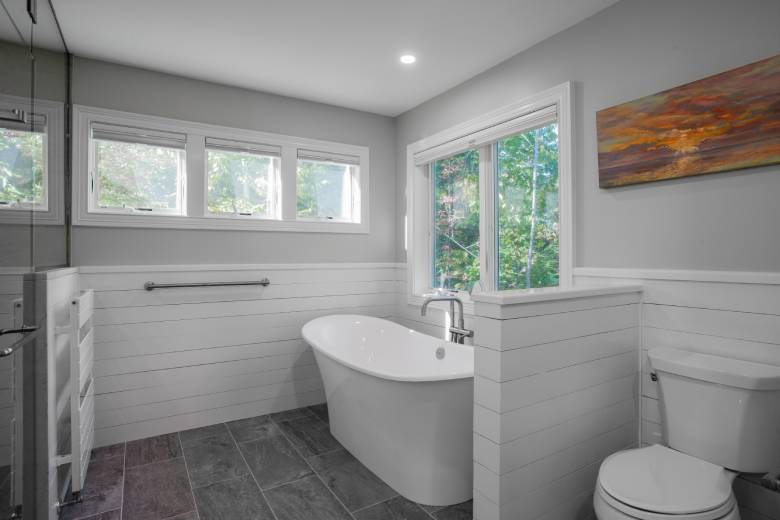 Bathroom remodel with free-standing tub and shiplap walls. Large gray tile floor, recessed lighting, and large windows with scenic view.