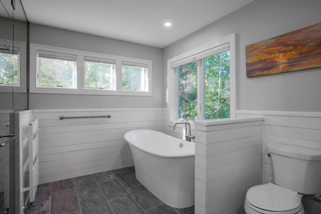 Modern bathroom remodel white shiplap and gray tile floor. White standing tub and recessed lights.