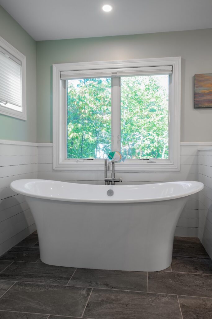 Remodeled tub in bathroom with gray tile flooring, large sliding window, and recessed lighting.