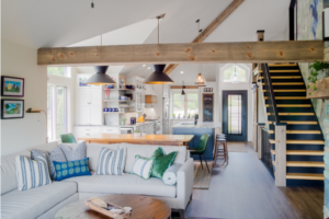 Remodeled living area with open-plan first floor, exposed beams and vaulted ceilings, and staircase leading upstairs.