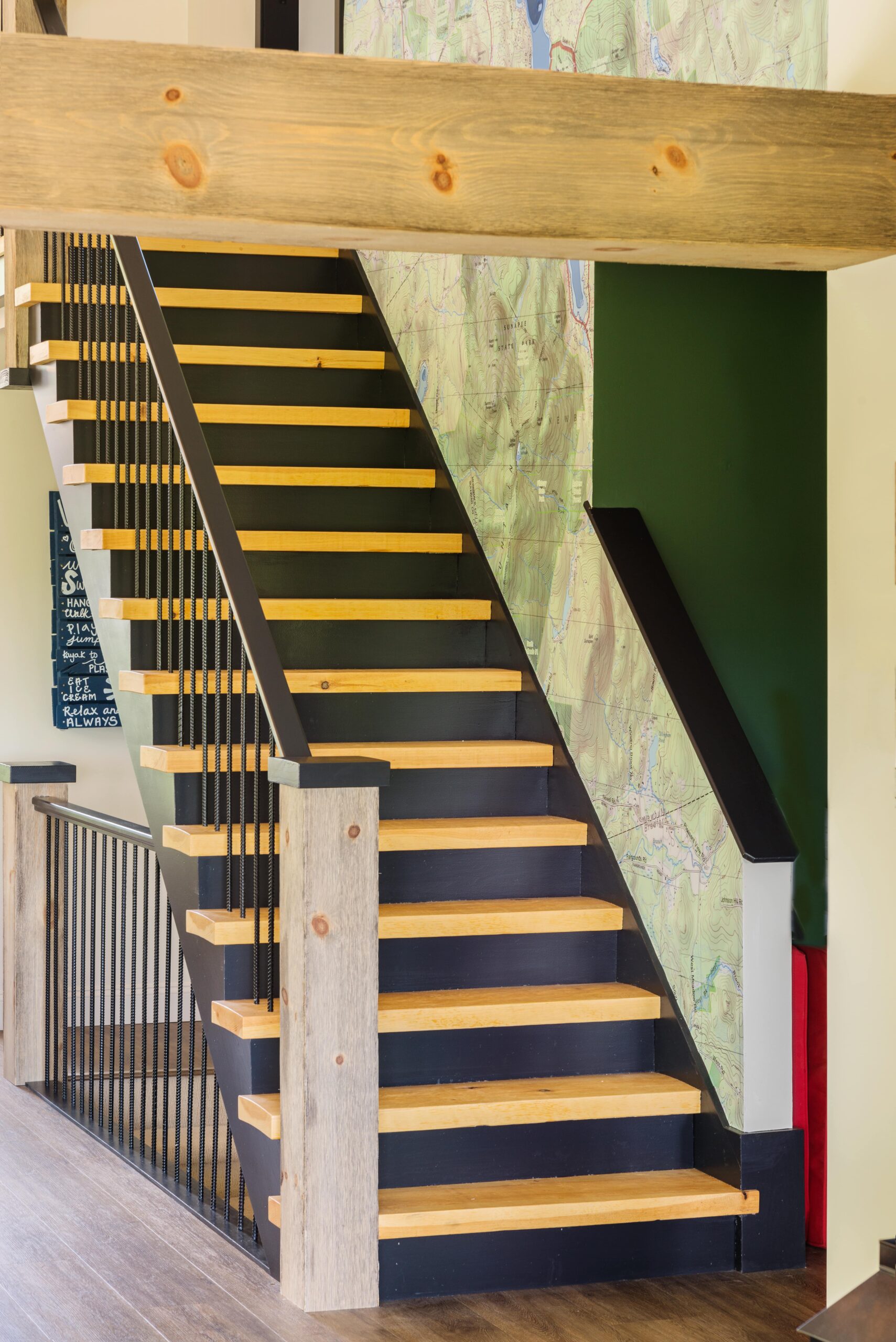 A wooden stair case with black railing and wood handrail, leading down to renovated living area.