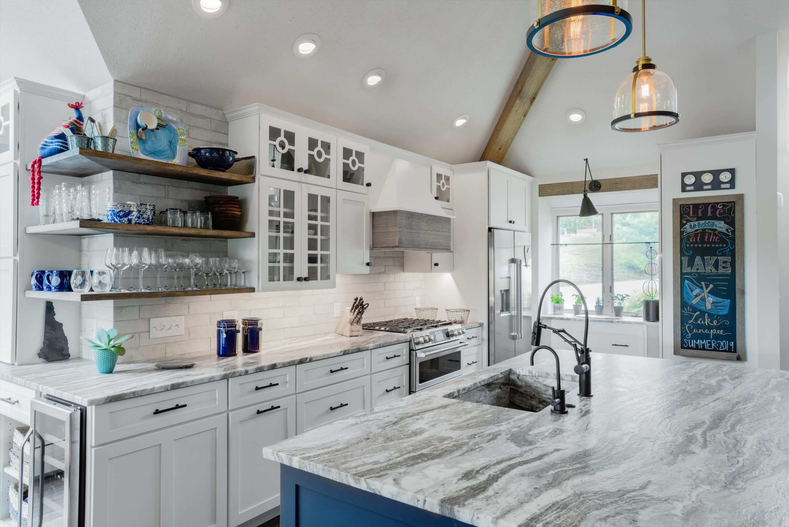 a spacious kitchen with marble counter tops and white cabinets. Open wood-slab shelving, recessed lights.