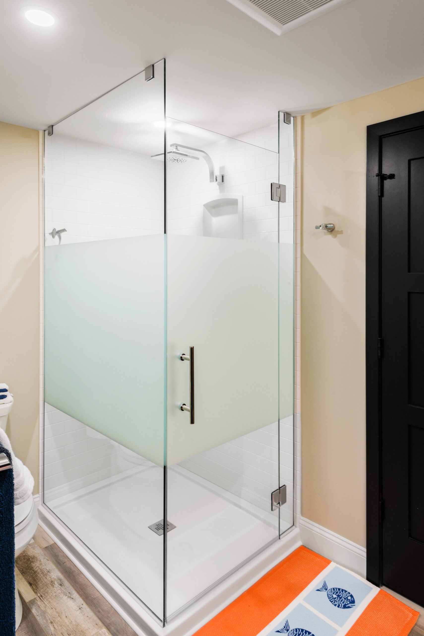 a bathroom with a glass shower and orange rug