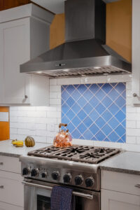 Remodeled kitchen with stainsteel gas stove and range hood, and custom blue tile backsplash.