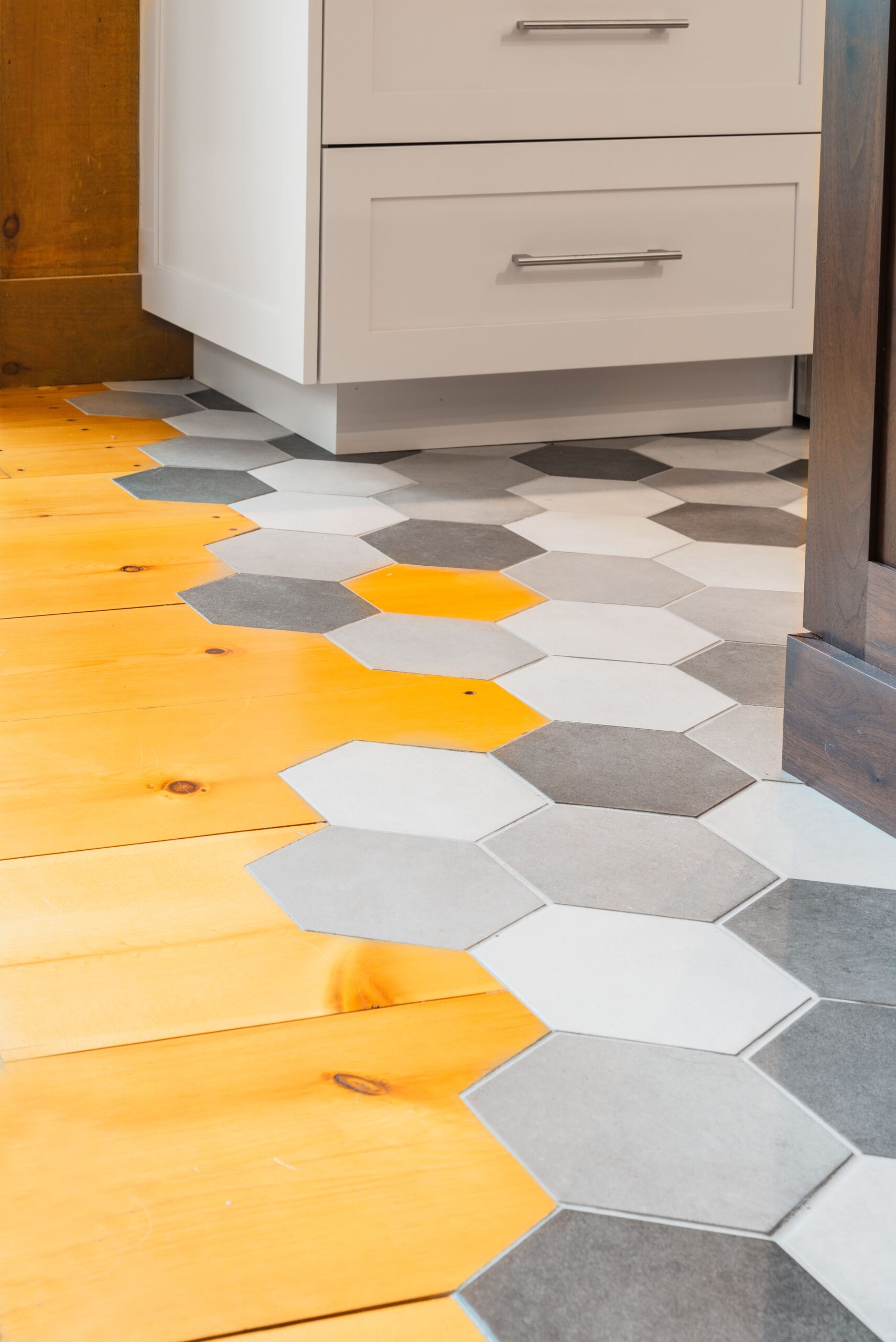 Kitchen flooring with gray honeycomb tile transitioning to wood