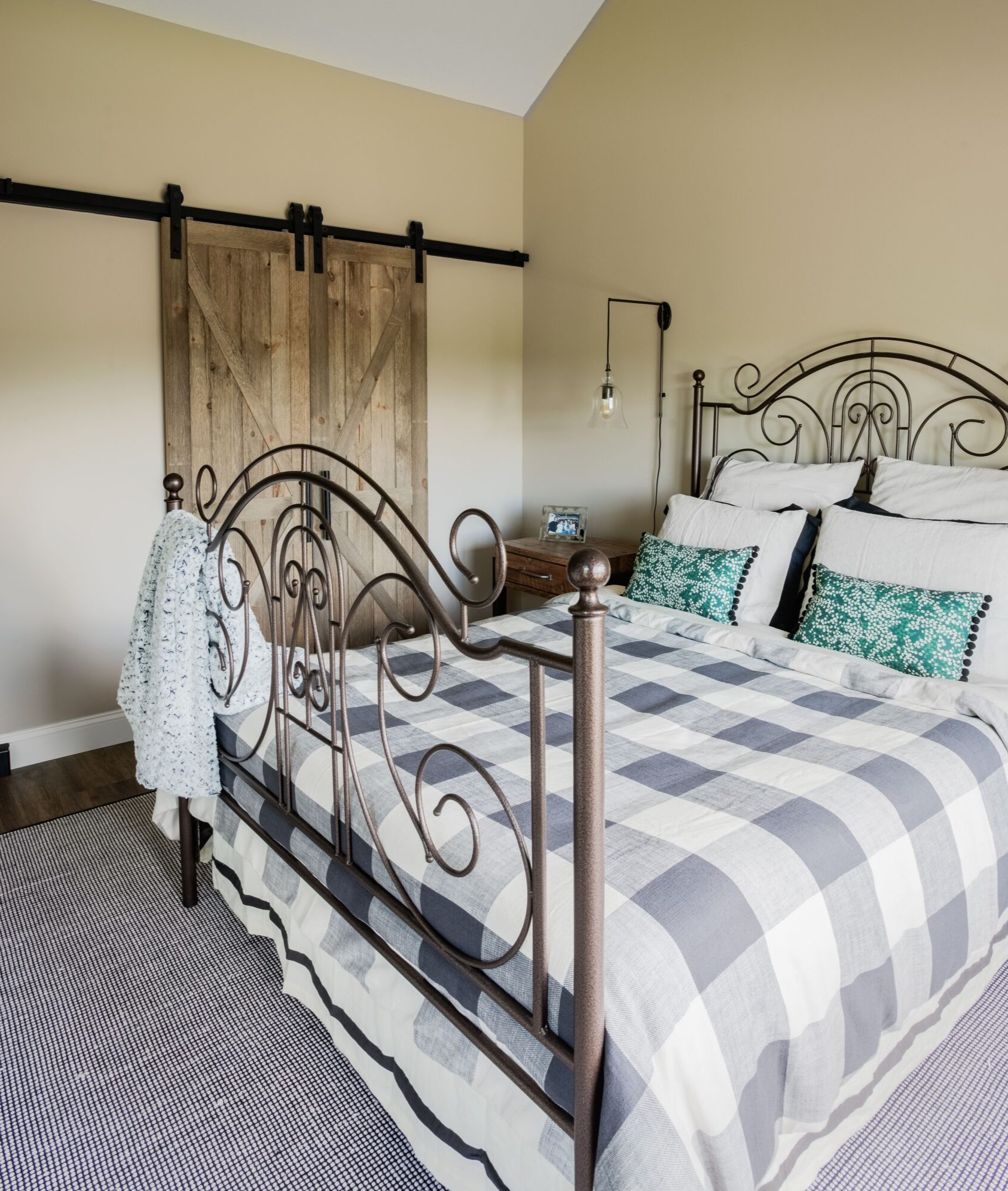 Remodeled bedroom with wood floors, light gray carpet, queen bed with metal decorative bed frame, and sliding woodgrain barn doors on other side of room.